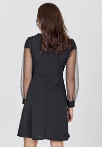 Black dress featuring sheer puff sleeves, a fitted bodice, and a flared skirt. Smooth texture with a concealed back zipper.
