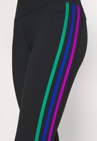 Leggings neri con tre strisce verticali verde, blu e viola lungo la cucitura esterna, realizzati in un tessuto elastico e liscio.
