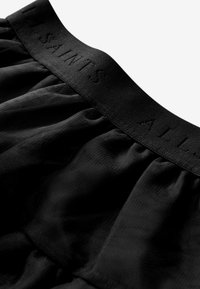 Cintura elastica nera con testo in rilievo "ALL SAINTS", attaccata a un tessuto leggero e texturizzato con dettagli arricciati.