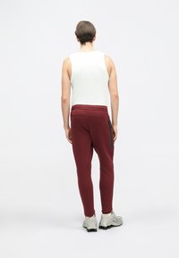 Bordo joggeri ar sašaurinātu piegriezumu, izgatavoti no mīkstas auduma, ar rāvējslēdzēja kabatu uz augšstilba un apvienoti ar baltu bezpiedurkņu topu.