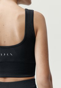 Čierny rebrovaný športový podprsenka so širokými ramienkami, s dizajnom výrezu na chrbte a s jemným logom na páske. Mäkkučký, pružný materiál.