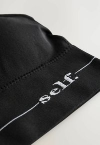 Mustvalge kangas kott sileda tekstuuriga, mille servas on valgete õmblustega tekst "self.", rõhutades minimalistlikku disaini.