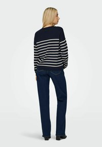 Maglione a righe blu Navy e bianche con scollatura rotonda, abbinato a jeans blu scuro e scarpe col tacco nere. La texture appare lavorata a maglia e liscia.