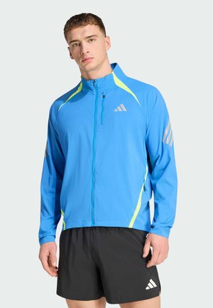 Blaue leichte Jacke mit halbem Reißverschluss, mit neongelben Akzenten und drei silbernen Streifen an den Ärmeln. Hergestellt aus atmungsaktivem Material.