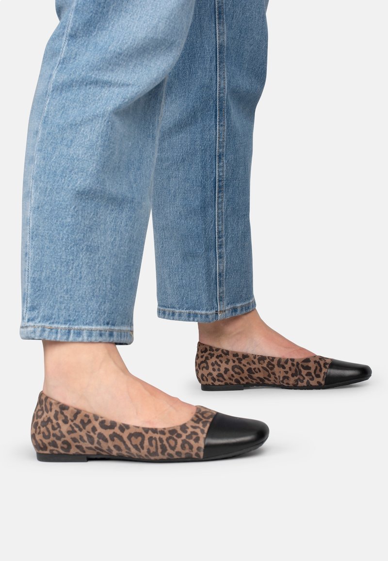 Ballerines imprimé léopard avec un bout en cuir verni noir ; dessus en tissu ; associées à un jean bleu clair avec revers.