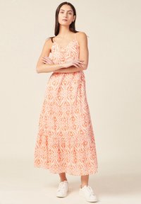 Maximekk dress with spaghetti straps, orange and white patterned fabric, tiered design, lightweight material, paired with white sneakers.