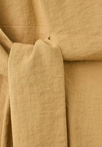 Tissu en lin beige noué en un nœud lâche, montrant la texture et les détails du tissage naturel.