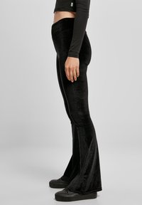 Musta samettiset leveälahkeiset housut, joissa on korkea vyötärö, sileä pinta ja aksenttisaumat. Yhdistetty mustiin, tasapohjaisiin kenkiin.