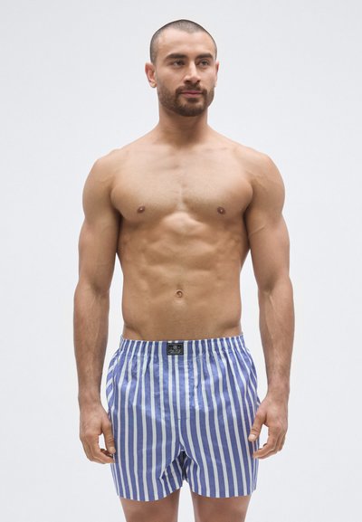 Pruhovan�é modro-biele trenky s elastickým pásom, vyrobené z ľahkej látky, s predným vreckom a štítkom na páse.