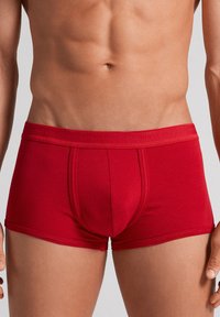 Boxer-culottes rouges en tissu lisse. Caractéristiques : coupe ajustée, poche fonctionnelle et ceinture élastique douce avec logo de la marque.