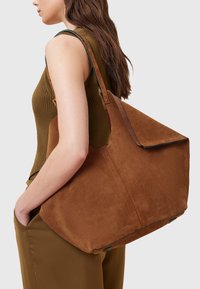 Borsa a tote in suede marrone con una forma strutturata, parte superiore piatta e dettagli in pelle. Di grandi dimensioni, con cuciture minime e una texture liscia.