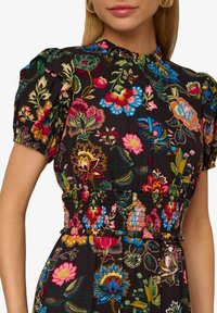 Bloemendress met een zwarte achtergrond, levendige multikleurige patronen, pofmouwen, smocktail en een hoge halslijn.