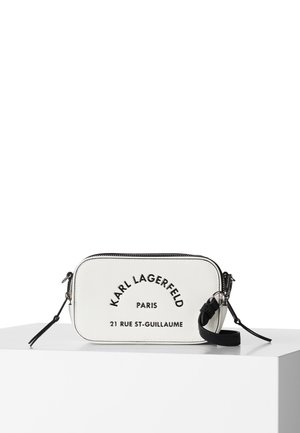 Biała prostokątna torba na ramię z czarnym zamkiem błyskawicznym, paskiem oraz wytłoczonym napisem KARL LAGERFELD Paris 21 Rue St-Guillaume na przodzie.
