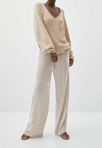 Beige knitted sweater with a V-neck, relaxed fit, and balloon sleeves, paired with light beige wide-leg trousers and brown sandals.
