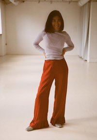 Raudonos plačios kelnės su raukšlėmis apačioje, derinamos su šviesiu ilgomis rankovėmis raukšlėtu marškinėliu. Apranga pasižymi laisvu siluetu ir neutralių spalvų palete.