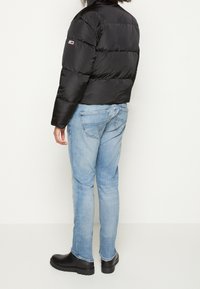 Doudoune noire avec un col haut et un design matelassé. Associée à un jean bleu clair et des bottines noires à enfiler.