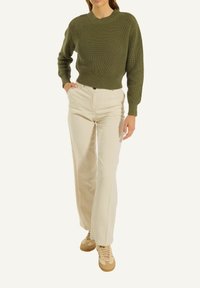 Olivgrüner, gerippter Strickpullover, beigefarbene, hochgeschnittene Hose und braune Sneaker. Der Pullover hat einen runden Ausschnitt und eine strukturierte Oberfläche.