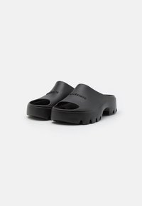 Mustat liukusandaalit avonaisilla varpailla, valmistettu sileästä kumista, jossa on paksu pohja, jossa on tekstuuri ja kohokuvioitu brändilogo.