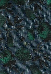 Mörkgrönt blommönster med blad vävt på en texturerad blå och svart rutig tygbakgrund.