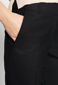 Czarne, dopasowane spodnie uszyte z gładkiej, teksturowanej tkaniny, wyposażone w boczne kieszenie i dopasowaną talię. Subtelne przeszycia dodają im struktury.