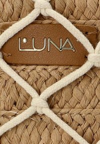 Bolso de paja tejido con una etiqueta de cuero marrón que muestra "LUNA" en letras metálicas, asegurado con acentos de cuerda trenzada blanca.
