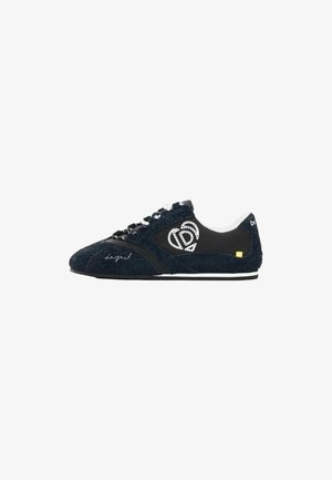 Svarte sneakers med lav profil og tekstureret stof, hvidt broderet hjerte-logo på siden, hvide snørebånd og tynd hvidstribet sål.
