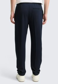 Marineblauwe, op maat gemaakte broek, gemaakt van gladde stof, met een enkele achterzak en een elastische tailleband voor comfort.