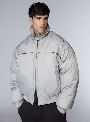 Giacca a vento grigio chiaro con collo alto, cerniera frontale e dettagli neri. Presenta un'imbottitura spessa e polsini a coste.