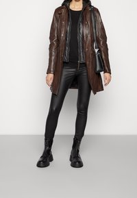 Brun läderjacka med en svart puffer-väst under, tillsammans med svarta läderleggings och svarta stövlar med dragkedja. Minimalistisk svart handväska.