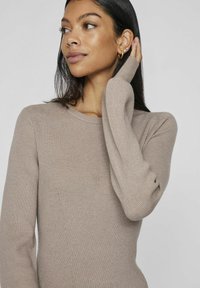 Maglione a coste beige con maniche lunghe, caratterizzato da un collo rotondo e una silhouette aderente. Dettagli delle cuciture sottili sul torso.