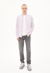 Hellblaues Button-up-Hemd über einem weißen T-Shirt, kombiniert mit grauen Jeans und grauen Sneakern. Das Outfit hat eine lässige Passform und ein elegantes Design.