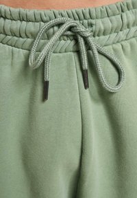 Lysegrønne sweatpants med en indsamlet elastisk talje og en flettet snor med plastikspidser, lavet af blødt bomuldsmateriale.