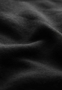Primo piano di tessuto nero con trama texture visibile e pieghe morbide che creano delicate ombre e luci.