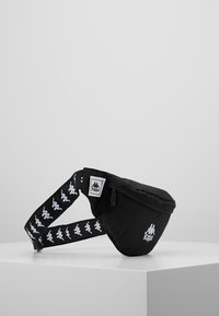 Czarna torba na pas o zakrzywionym kształcie, z zamykaną kieszenią i regulowanym pasek z białym wzorem logo i brandingiem.