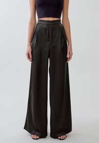 Pantaloni a gamba larga in tessuto scuro con una texture liscia e lucida. Design a vita alta con pieghe e tasche laterali.