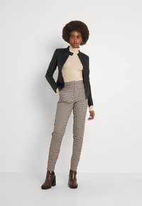 Svart skinnjakke, beige rullekragegenser og brune rutete bukser. Modellen har på seg boots med tykk hæl, som fremhever et slankt, tettsittende utseende.