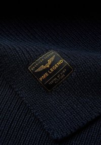 Marine gebreide trui met een gestructureerde afwerking en een rechthoekig stoffen label met gouden lettering en een adelaarembleem.