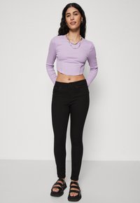 Ibolya színű, hosszú ujjú crop top, texturált anyagból, fekete skinny farmerral és fekete szandálokkal, amelyeken több pánt található.