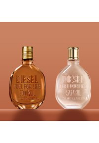 Dos botellas de perfume Diesel Fuel For Life de 50 ml con tapones dorados, una ámbar y otra transparente, sobre una superficie marrón con un fondo marrón.
