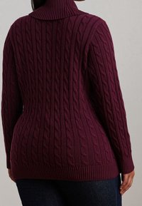 Burgundy cable-knit sweater with a high collar, ribbed hem, and textured pattern, shown from the back, paired with dark denim.