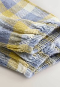 Kék, sárga és fehér kockás mintájú flanel anyag. Ráncolt mandzsettával rendelkezik, amelyen látható varrások és texturált felület található.
