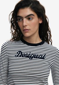 Pruhovaná dlhá rukávová košeľa v bielej a čiernej farbe; obsahuje námornícke vyšívané logo "Desigual" na hrudi; okrúhly golier; jemný materiál.