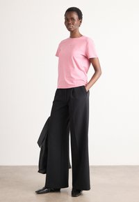 Lyserød bomulds t-shirt med korte ærmer og rund hals, parret med brede sorte bukser og sorte sko, med en blazer draperet i nærheden.