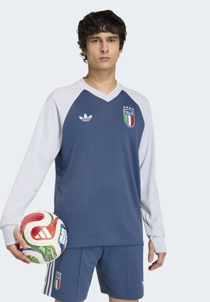 Ung mand i italiensk fodboldtrøje, der holder en flerfarvet Adidas fodbold mod en ensfarvet baggrund.