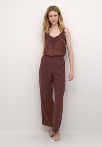 Bordový saténový top s krajkovými detaily, spárovaný s širokými bordovými kalhotami. Hladká textura, neutrální podpatky dokončují outfit.