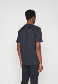 Tricou din bumbac negru cu mâneci scurte, decolteu rotund și un design texturat pe spate. Croială ușor ajustată, asortat cu o pereche de pantaloni care se potrivesc.