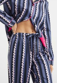 Marineblauw en paarse gestreepte pyjama-set met zigzagpatronen, bestaande uit een knoopsluiting bovenstuk en een broek met trekkoord,accentueert met roze afwerking.