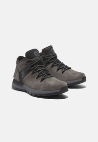 Botas de senderismo en ante gris con detalles en negro, que cuentan con un collar acolchado y múltiples ojales para los cordones, diseñadas para la durabilidad y el agarre.