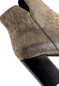 Botín de tobillo dorado con un alto tacón negro. La superficie presenta un patrón de cuadrícula y un diseño de parte superior abierta.