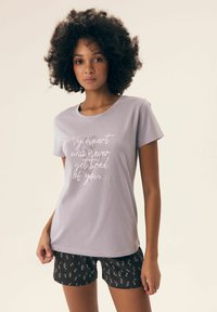 Jasnofioletowa koszulka z krótkim rękawem z białym nadrukiem. Czarne szorty z małym białym wzorem, wygodny krój i miękka tkanina.